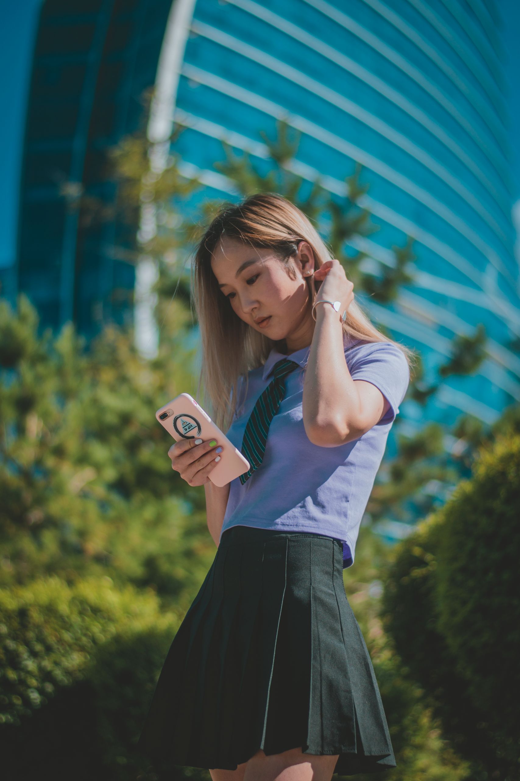A young woman checks her phone outdoors against a modern architectural background in Ulaanbaatar, Mongolia.
